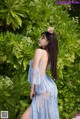 A woman in a blue dress standing in front of a bush.