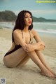 A woman in a black bathing suit sitting on a beach.