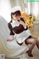 A woman in a maid outfit sitting on a bed.