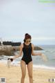 A woman in a black bathing suit standing on a beach.