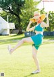 A woman in a green bikini and a straw hat is dancing in the grass.